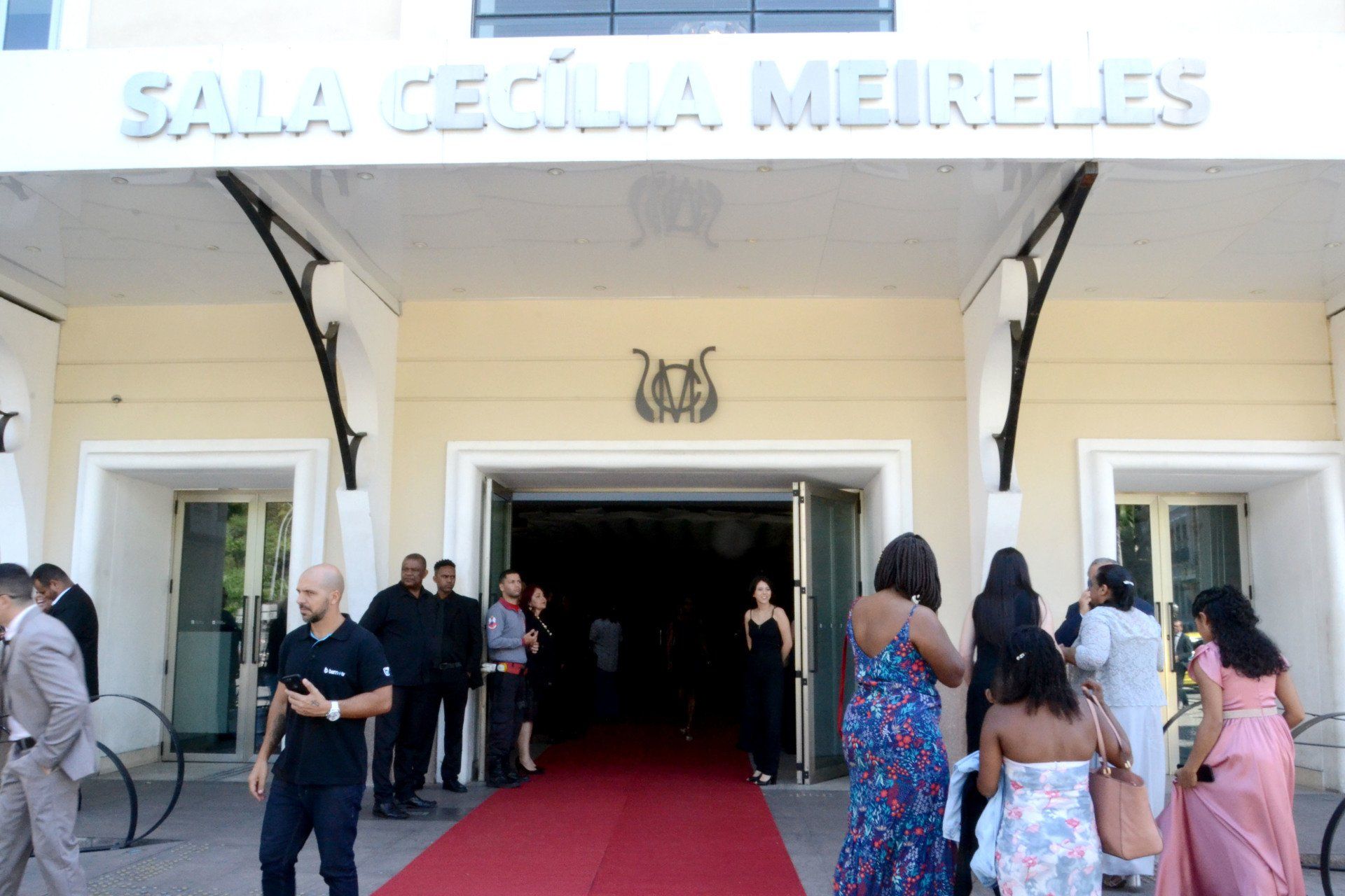 Um grupo de pessoas está em frente a um prédio que diz sala cecilia mereles