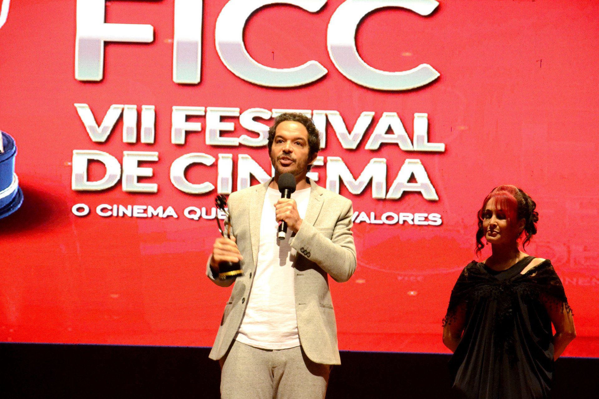 Um homem está fazendo um discurso em frente a uma tela que diz ficc