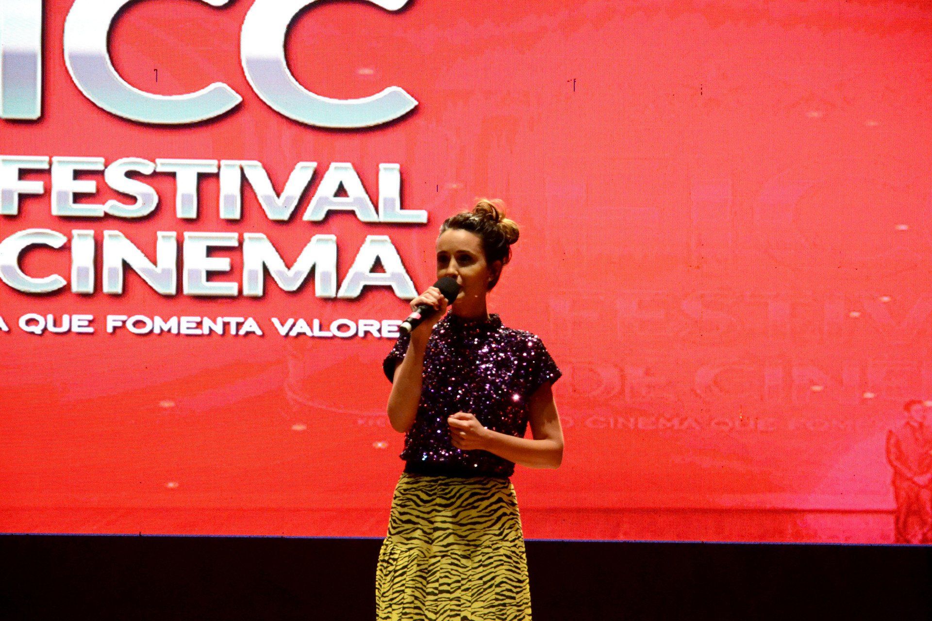 Uma mulher cantando em um microfone em frente a uma placa de cinema de festival