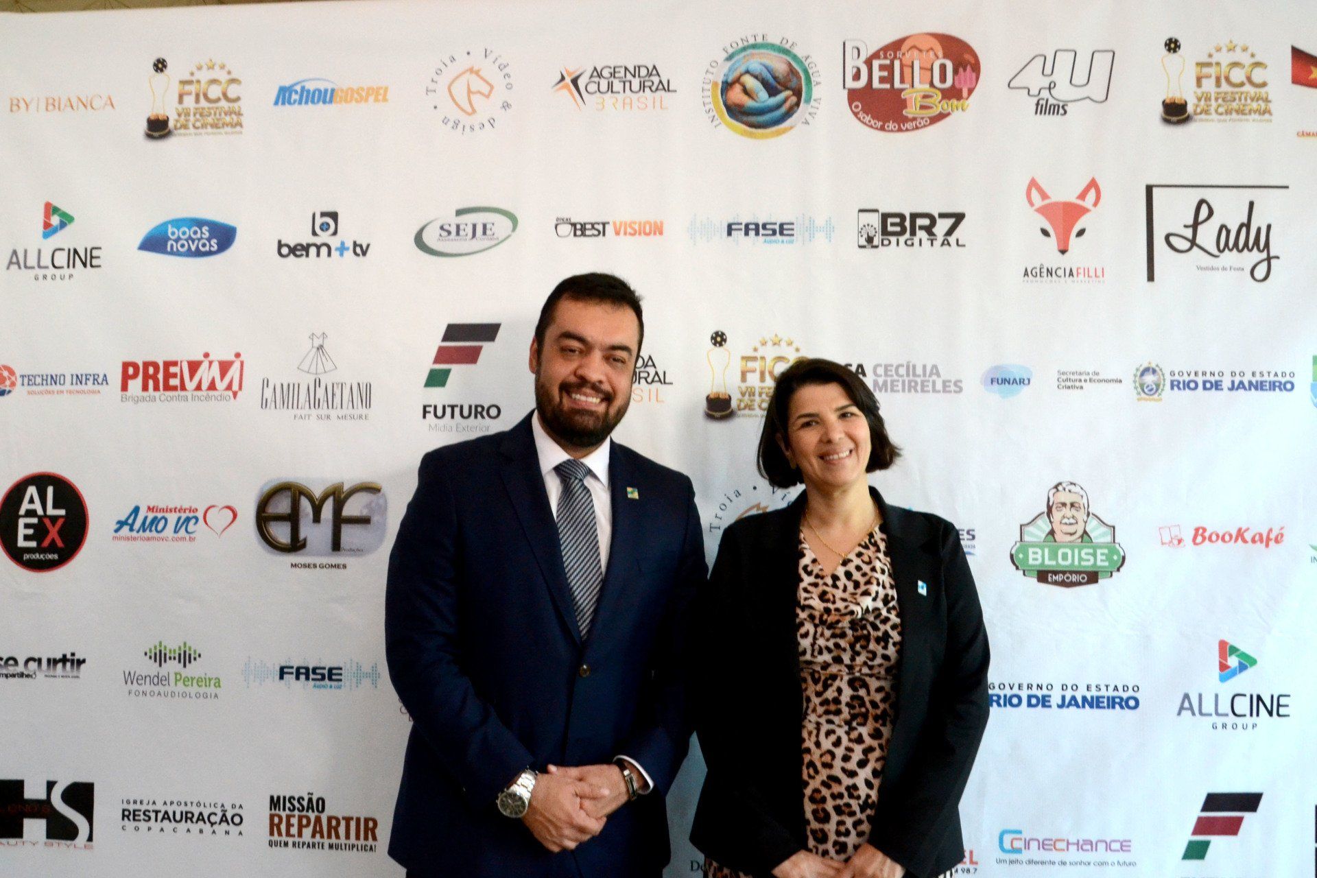 Um homem e uma mulher estão em pé em frente a uma parede com logotipos.