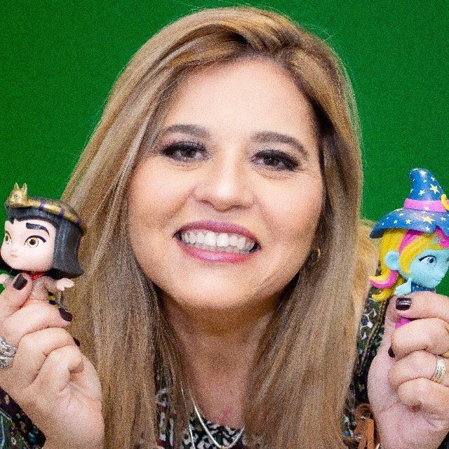 Uma mulher está segurando duas bonecas nas mãos e sorrindo.