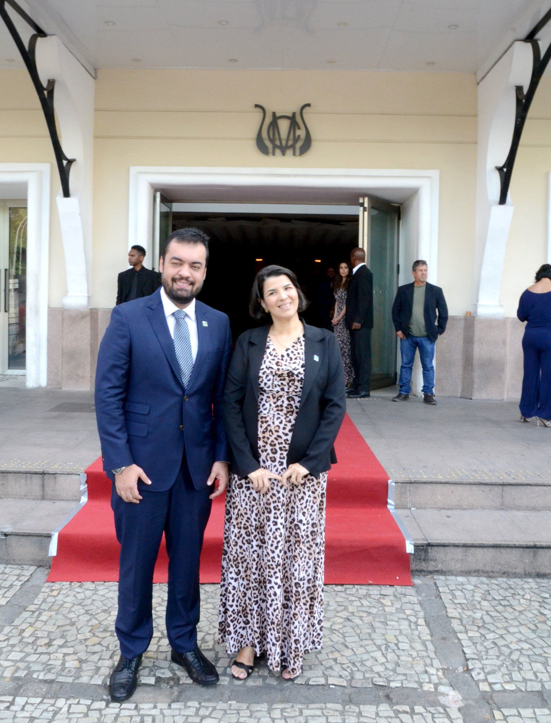 Um homem de terno e gravata está ao lado de uma mulher de vestido em um tapete vermelho