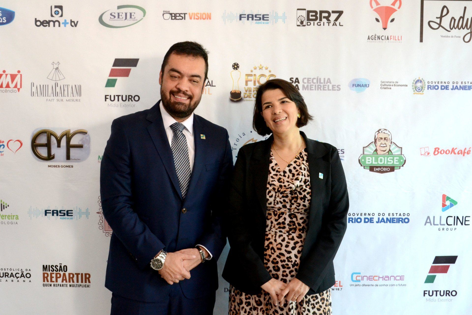 Um homem e uma mulher estão em pé em frente a uma parede com logotipos.