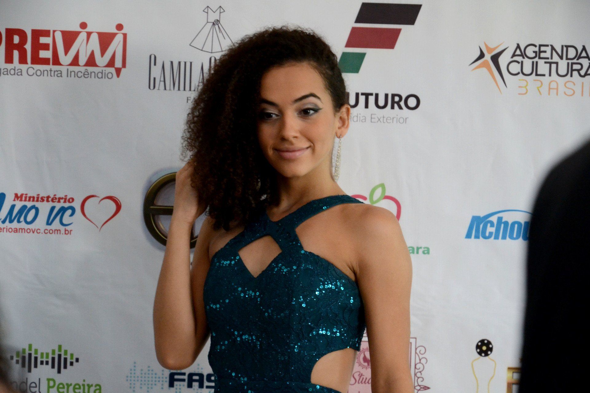 Uma mulher de vestido azul está parada em frente a uma parede com logotipos