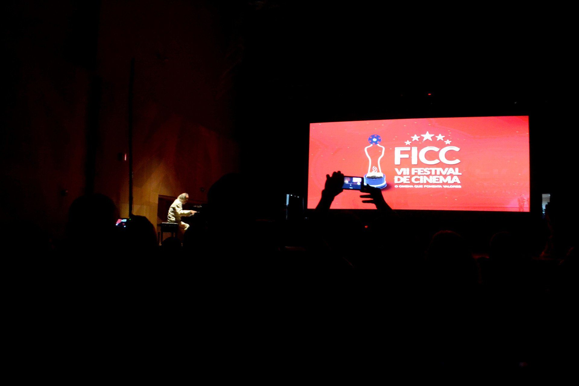 Um homem está sentado em frente a uma tela grande que diz ficc