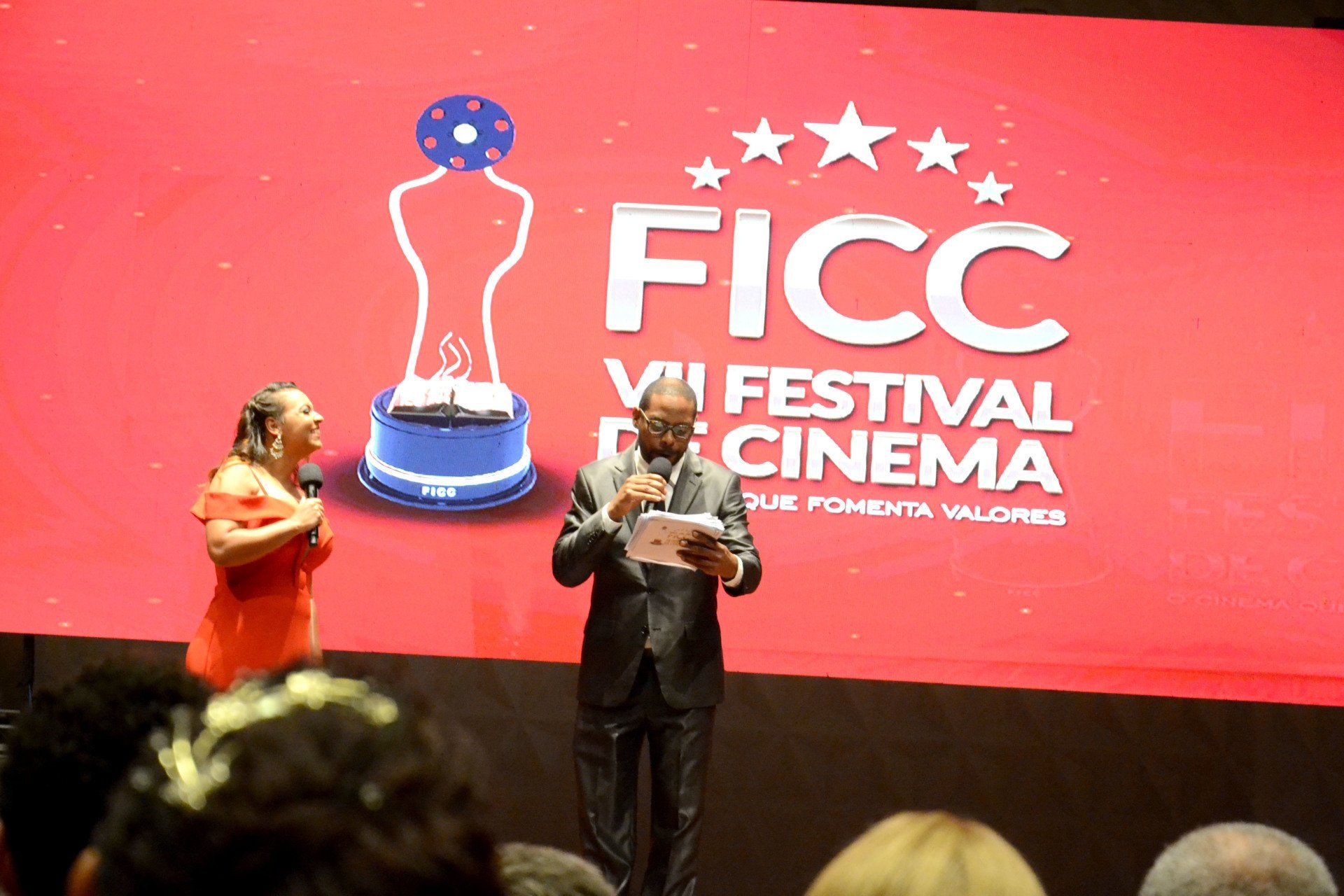 Um homem e uma mulher estão em pé em frente a uma tela que diz cinema festival ficc
