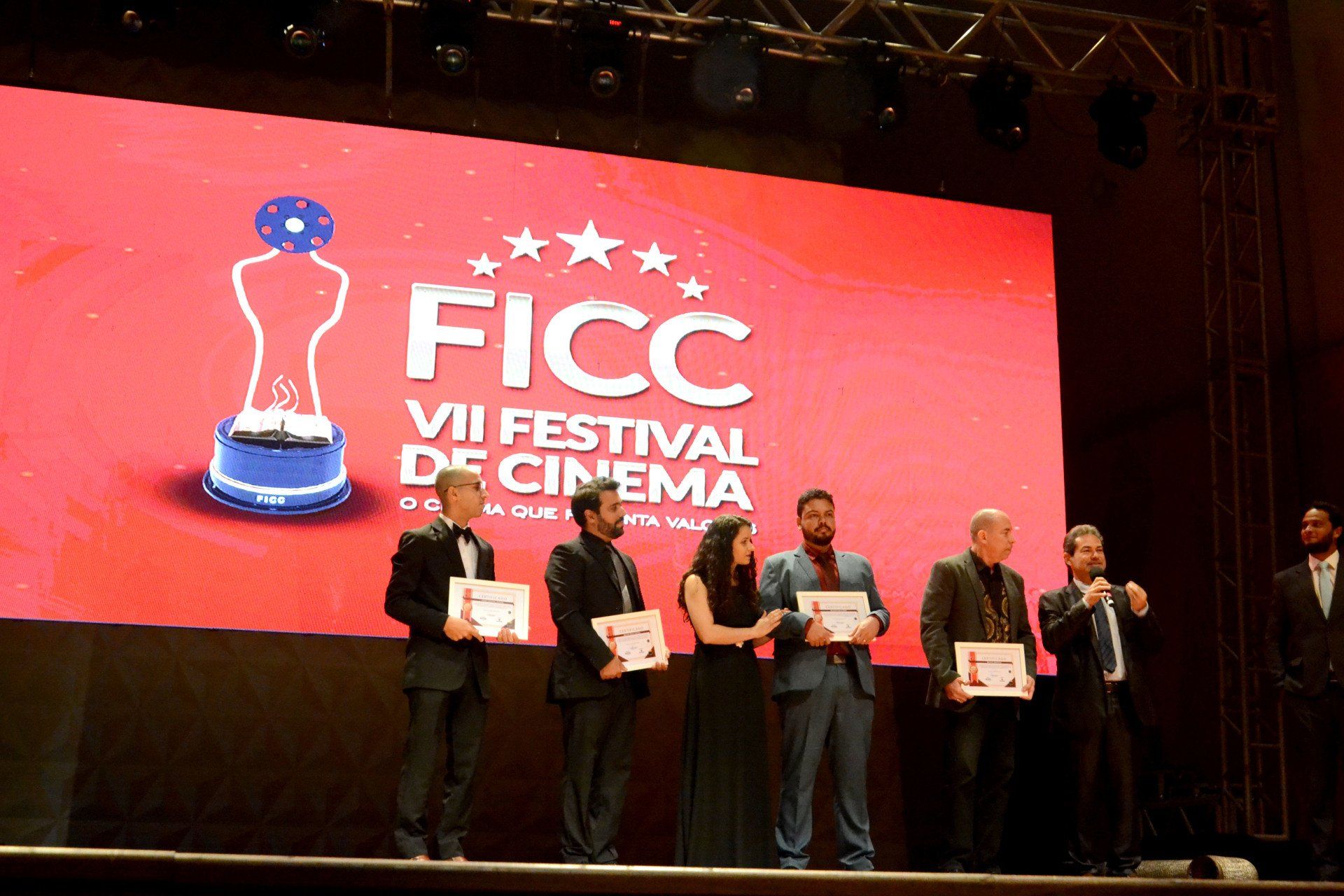 Um grupo de pessoas em pé na frente de uma tela que diz ficc