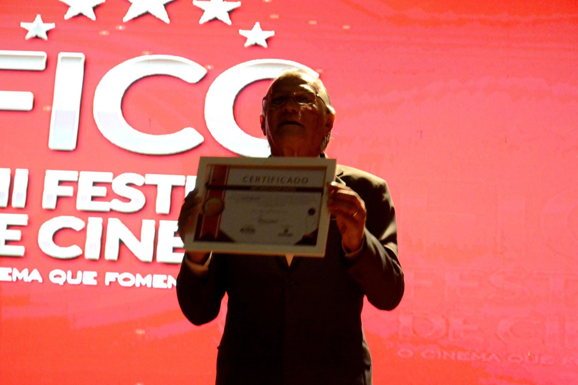 Um homem segurando um certificado em frente a uma tela que diz fico