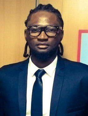 Um homem de terno e gravata usa óculos e dreadlocks.