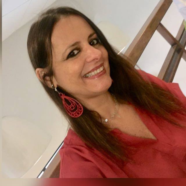 Uma mulher vestindo uma camisa vermelha e brincos vermelhos sorri para a câmera