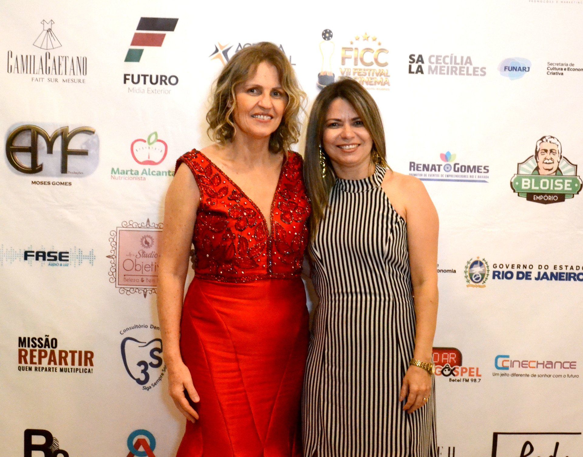 Duas mulheres estão posando para uma foto em frente a uma parede com logotipos.
