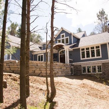 A large blue house is surrounded by trees and dirt