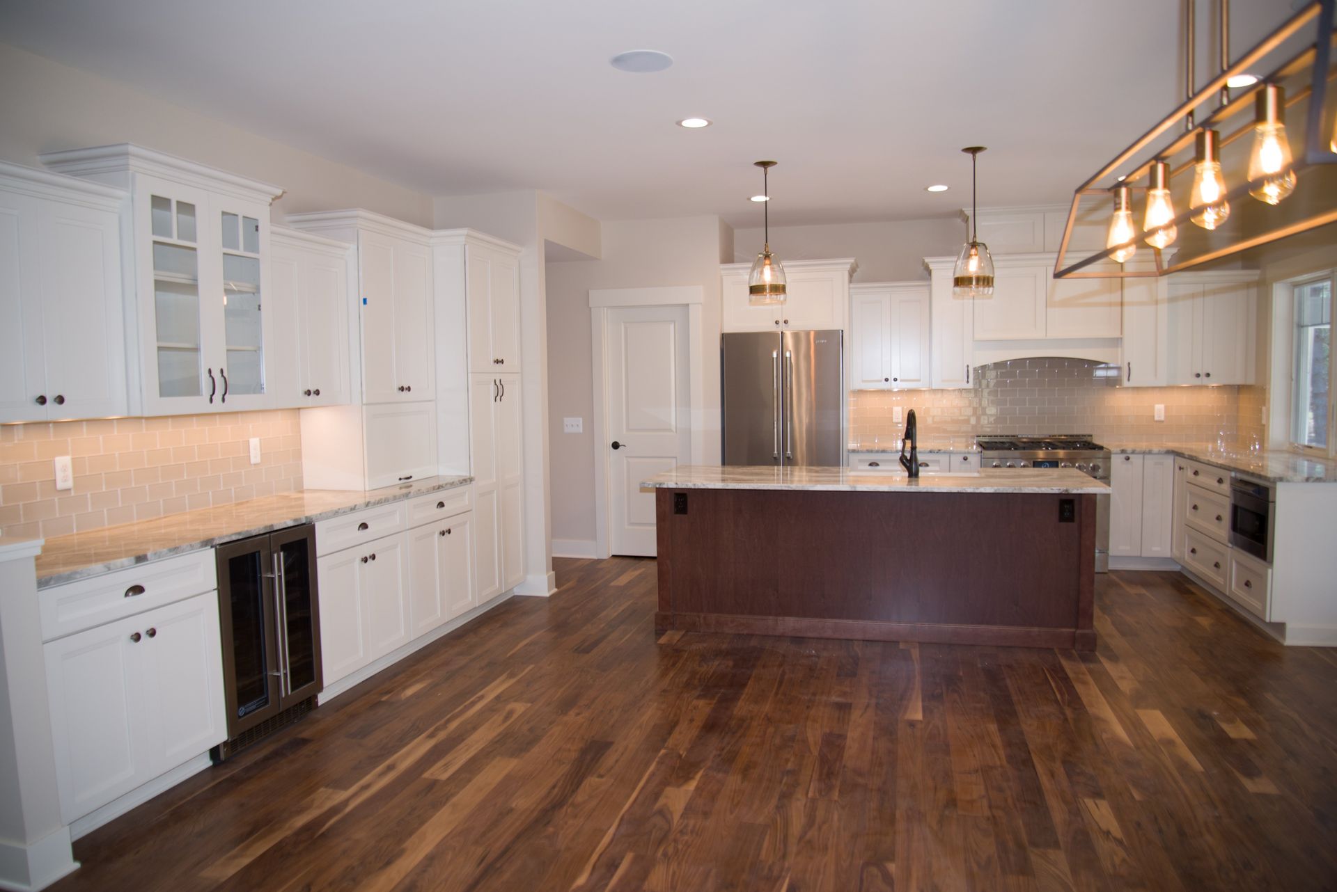 A large empty kitchen with white cabinets and hardwood floors.