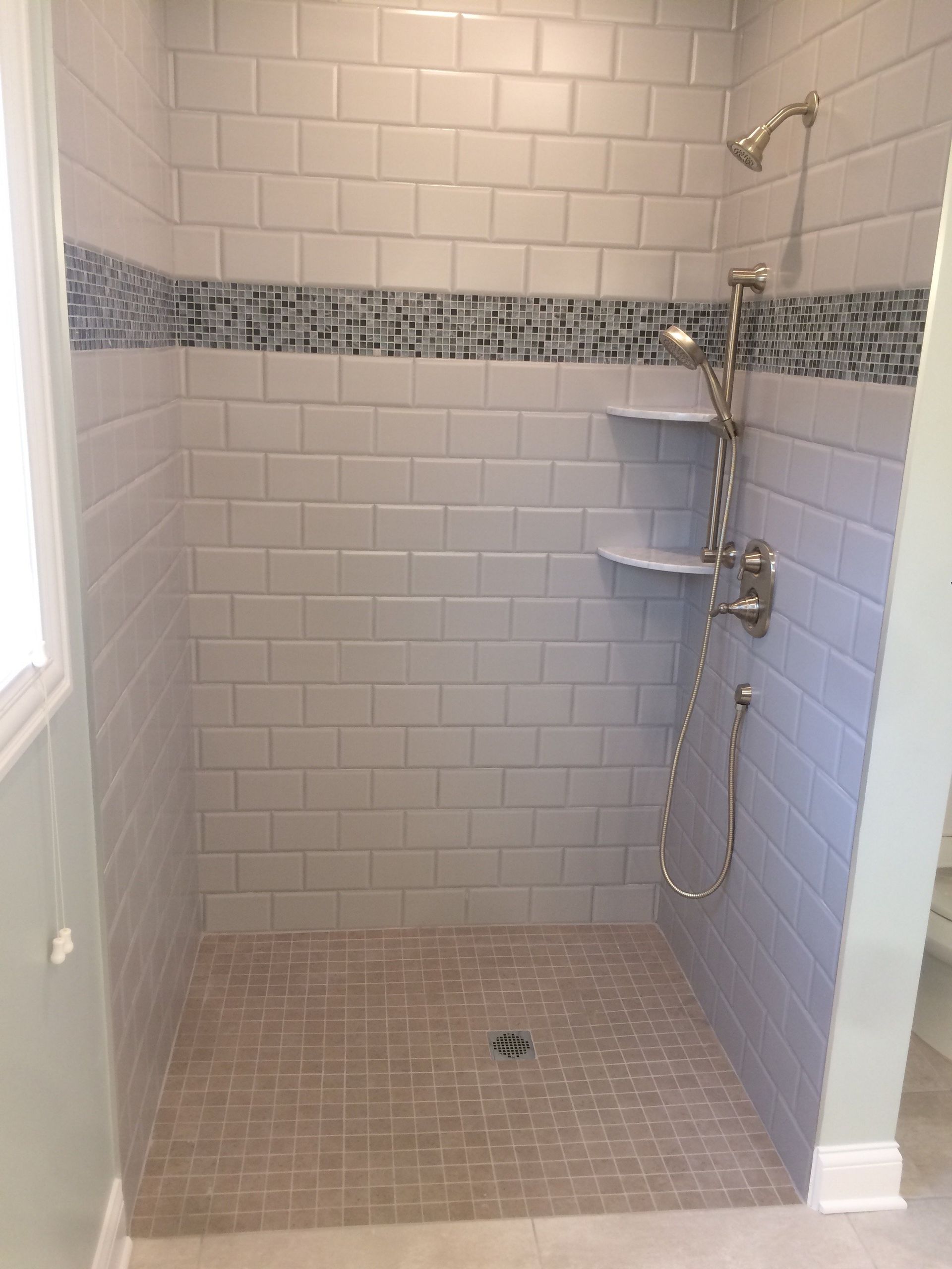 A walk in shower with white tiles and a mosaic border.