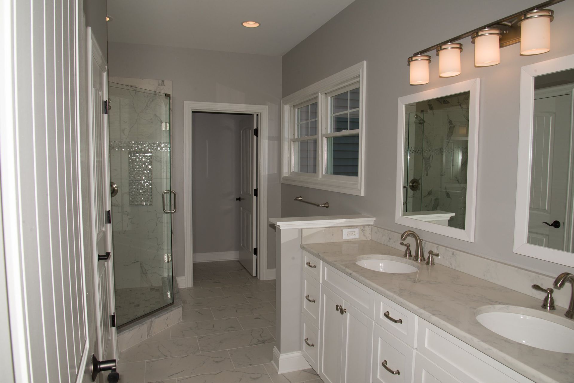 A bathroom with two sinks , two mirrors and a walk in shower.