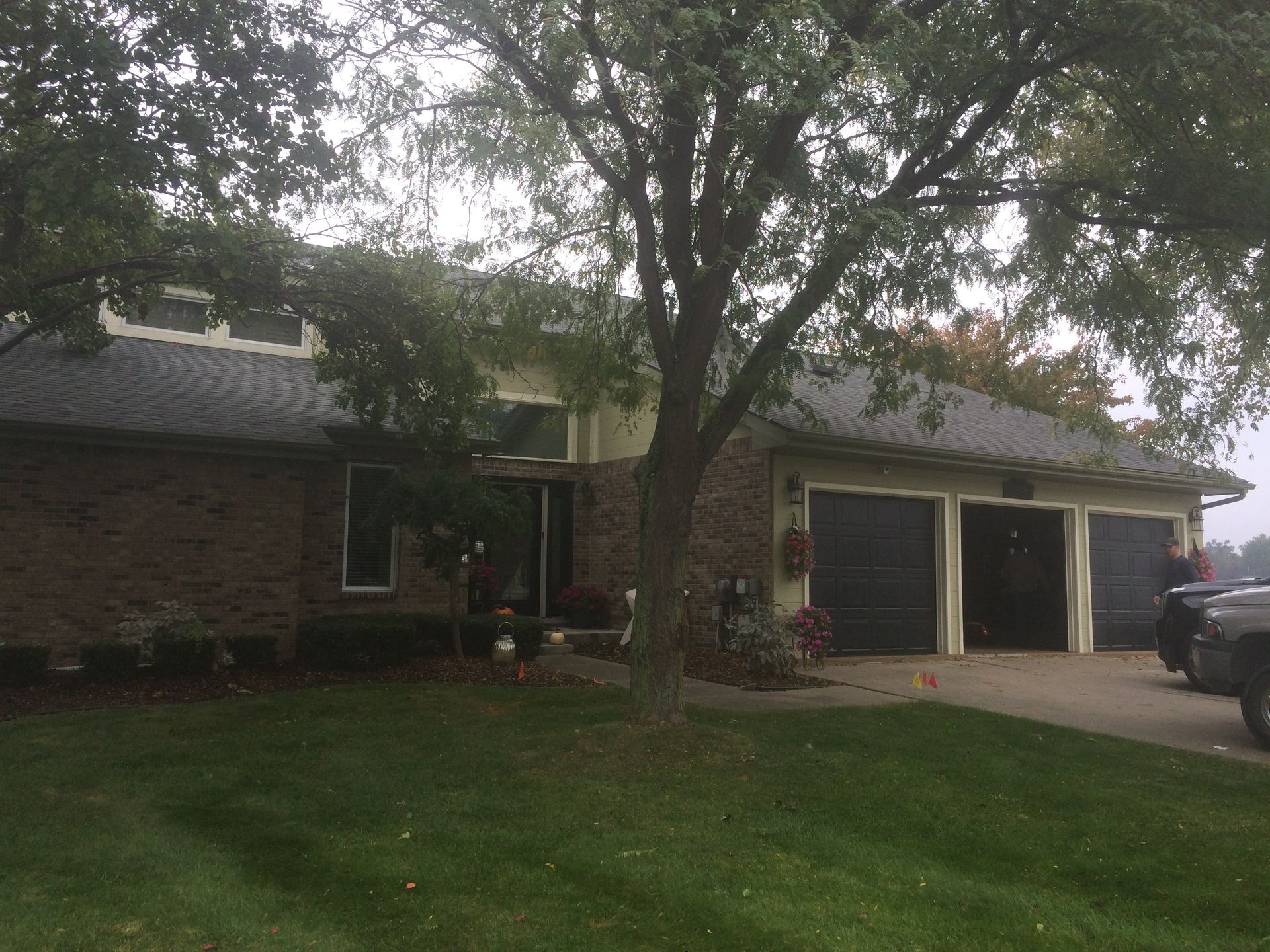 A brick house with two garages and a tree in front of it.
