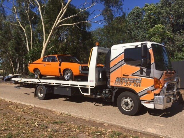 Orange Tow Truck Carrying an Orange Car on a Roadside With Trees in the Background — A1 Panel & Paint In Emerald, QLD