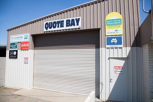Quote Bay Storefront With Closed Roller Door and Service Signs on a Beige Industrial Building — A1 Panel & Paint In Emerald, QLD