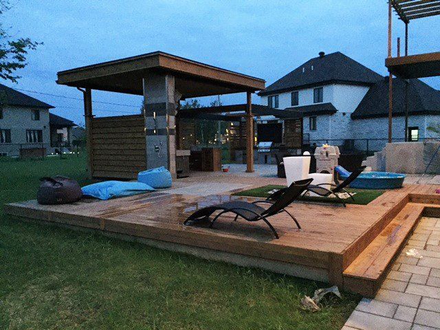 Une terrasse en bois avec des chaises et un gazebo dans la cour
