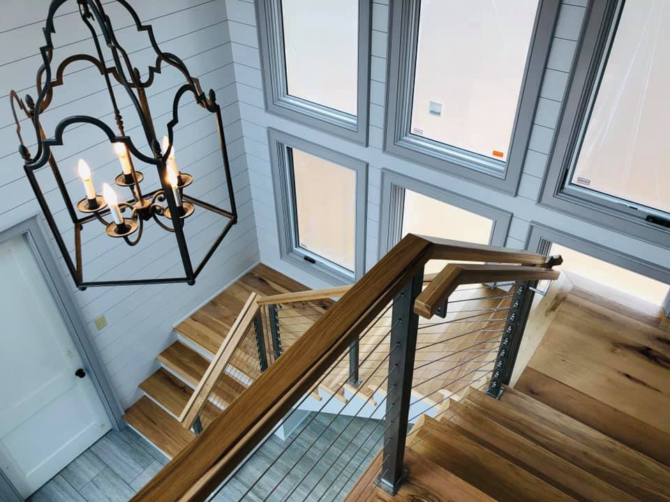 Staircase with stainless cable railing and wood handrail beside a wall of windows, Greenville SC