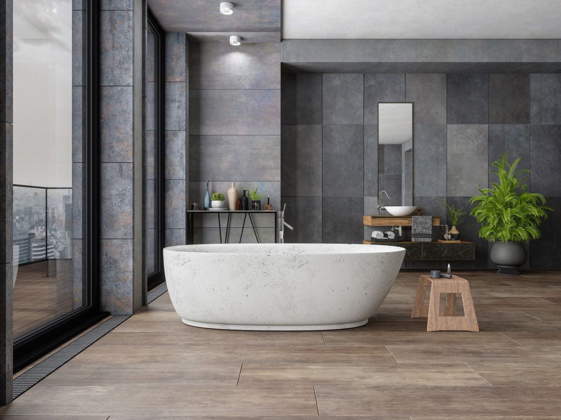 Bagno moderno con piastrelle grigie, vasca da bagno indipendente, pavimenti in legno e ampia finestra.