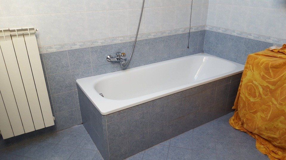 Vasca da bagno in un bagno con piastrelle blu e un asciugamano giallo.