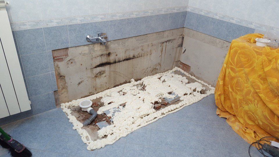Bagno in fase di ristrutturazione, con parete esposta dietro una vasca da bagno parzialmente installata e schiuma rovesciata.