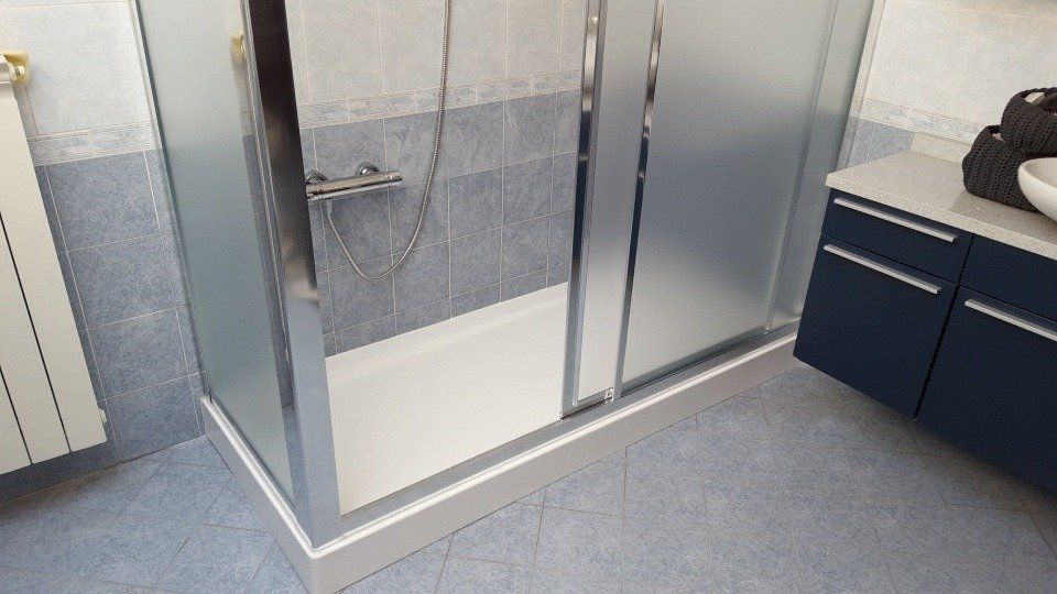 Bagno moderno con doccia, mobile lavabo, pareti piastrellate blu e pavimento grigio.