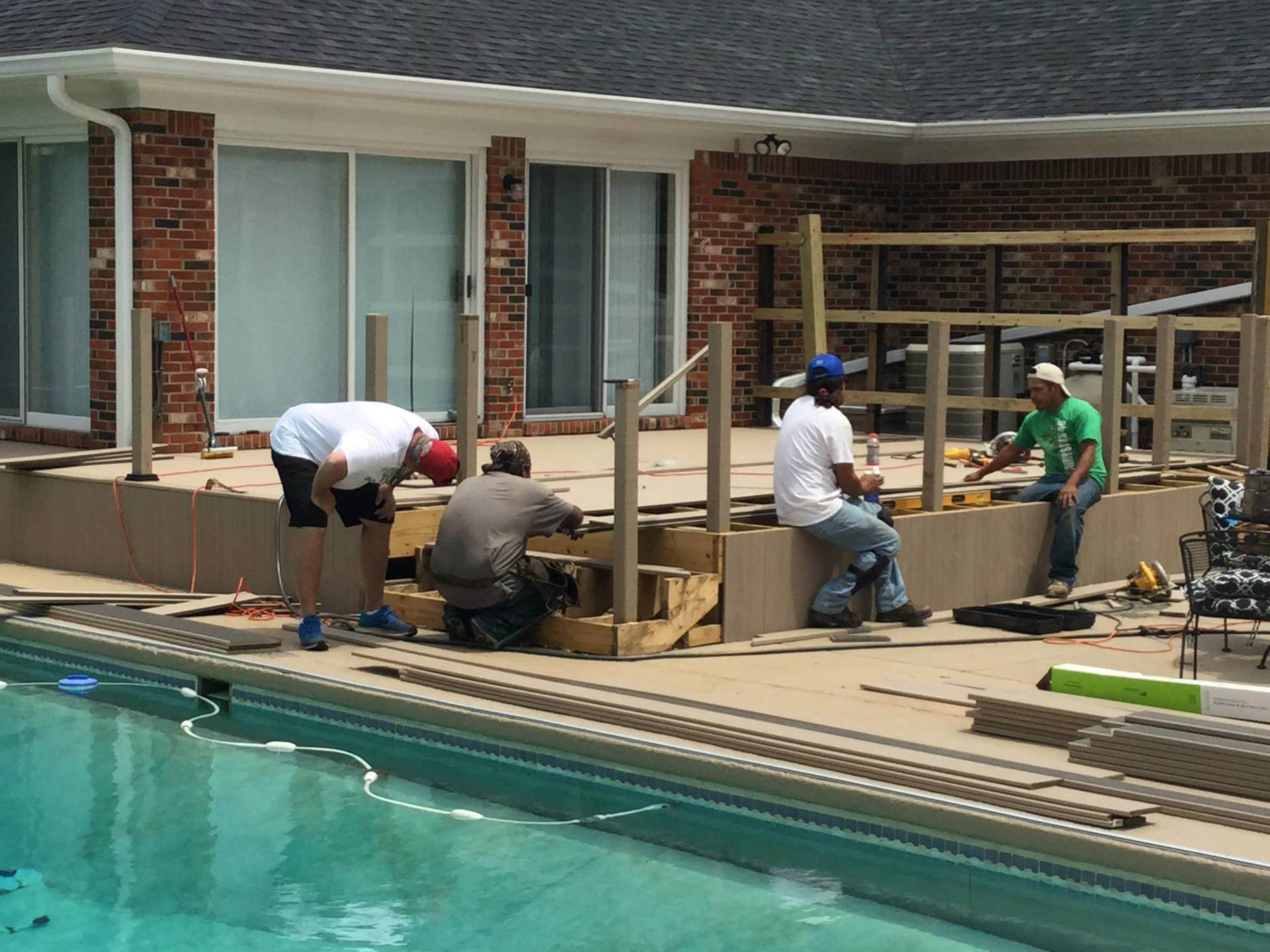 Workers building a wooden deck beside a swimming pool and brick house