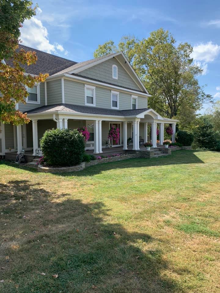 Gray two-story house with white trim, front porch, and large lawn in a sunny suburban yard