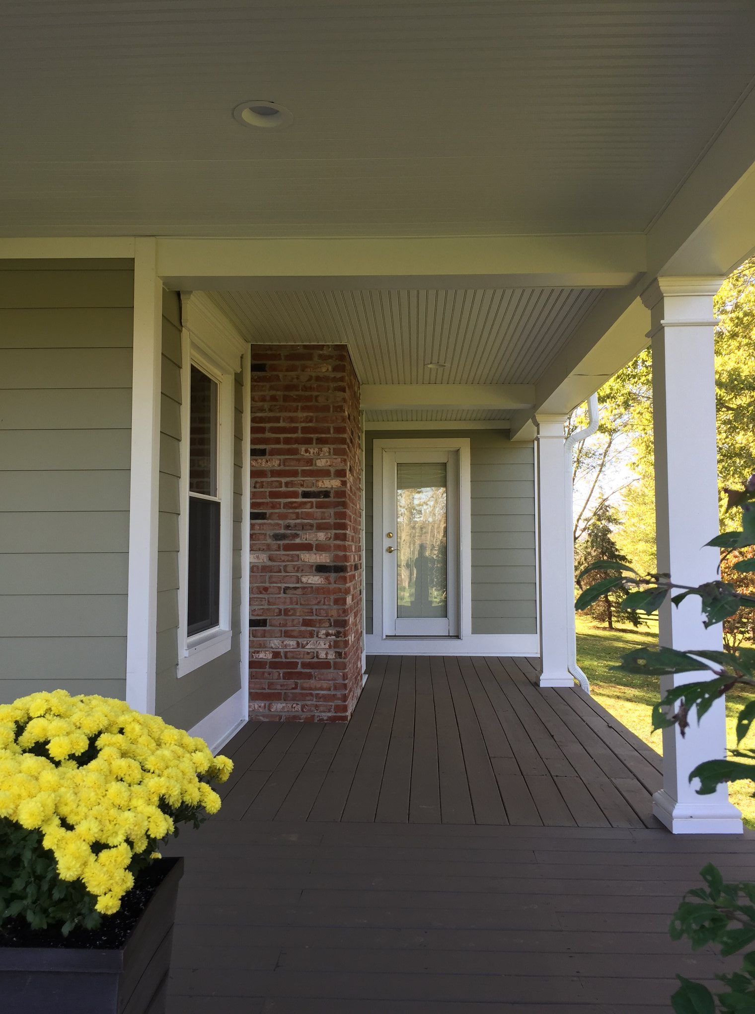 Covered front porch with white siding, brick wall, and yellow flowers by the steps.