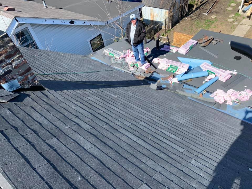 Worker on a rooftop installing pink insulation boards beside a blue building.