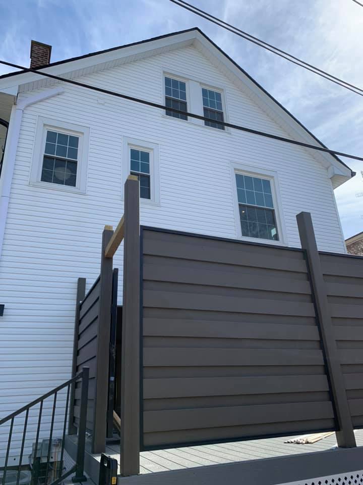 A white-sided house with a modern, brown horizontal-slatted privacy fence on a deck.