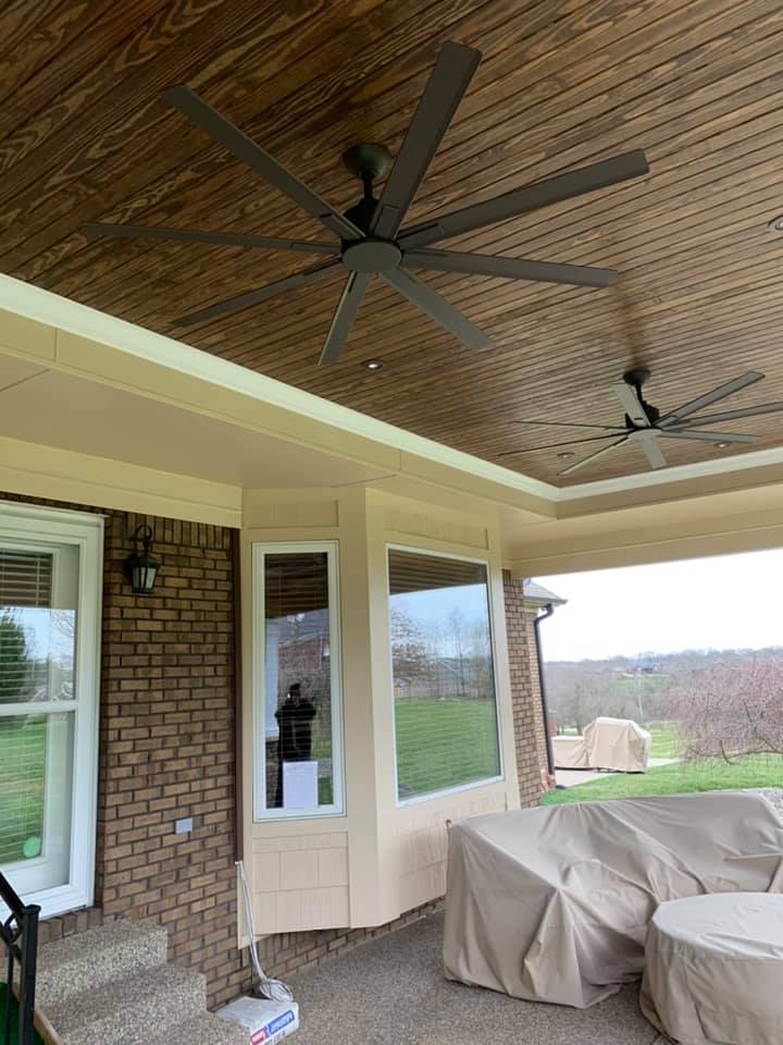 Covered patio with two ceiling fans, brick wall, windows, and a grill covered by a tarp.