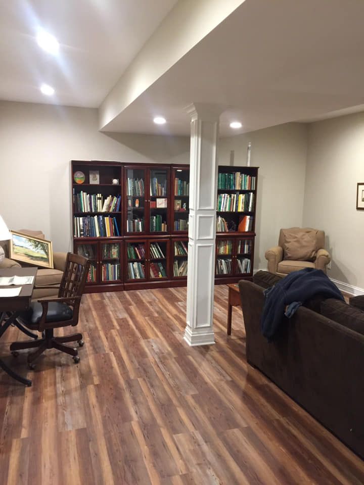 Home office with bookshelves, desk, chair, and a brown couch in a basement-like room