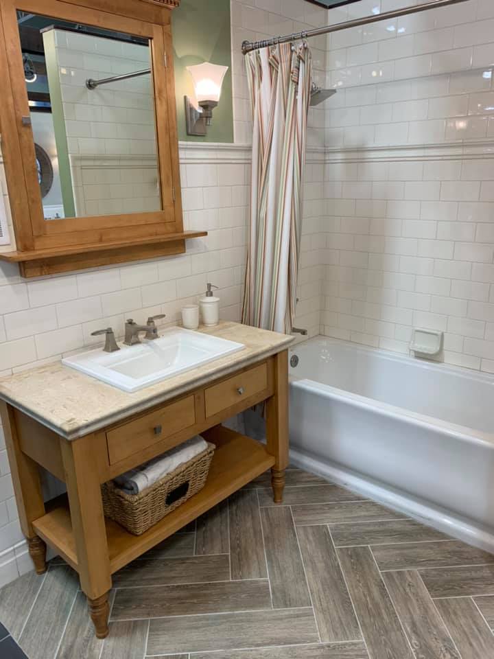 Bathroom with wooden vanity, white sink, mirror, tiled shower, and bathtub.