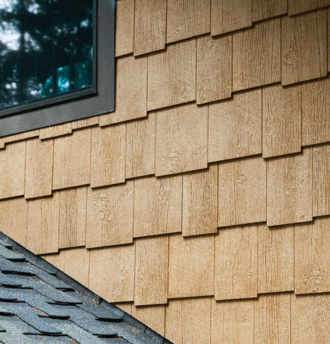 Close-up of tan cedar shingle siding beside a dark-framed window and gray roof shingles