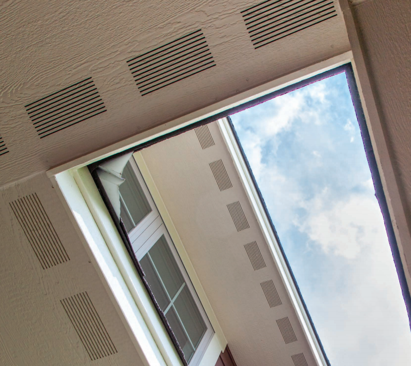 Upward view of a building facade with windows, soffits, and blue sky with clouds