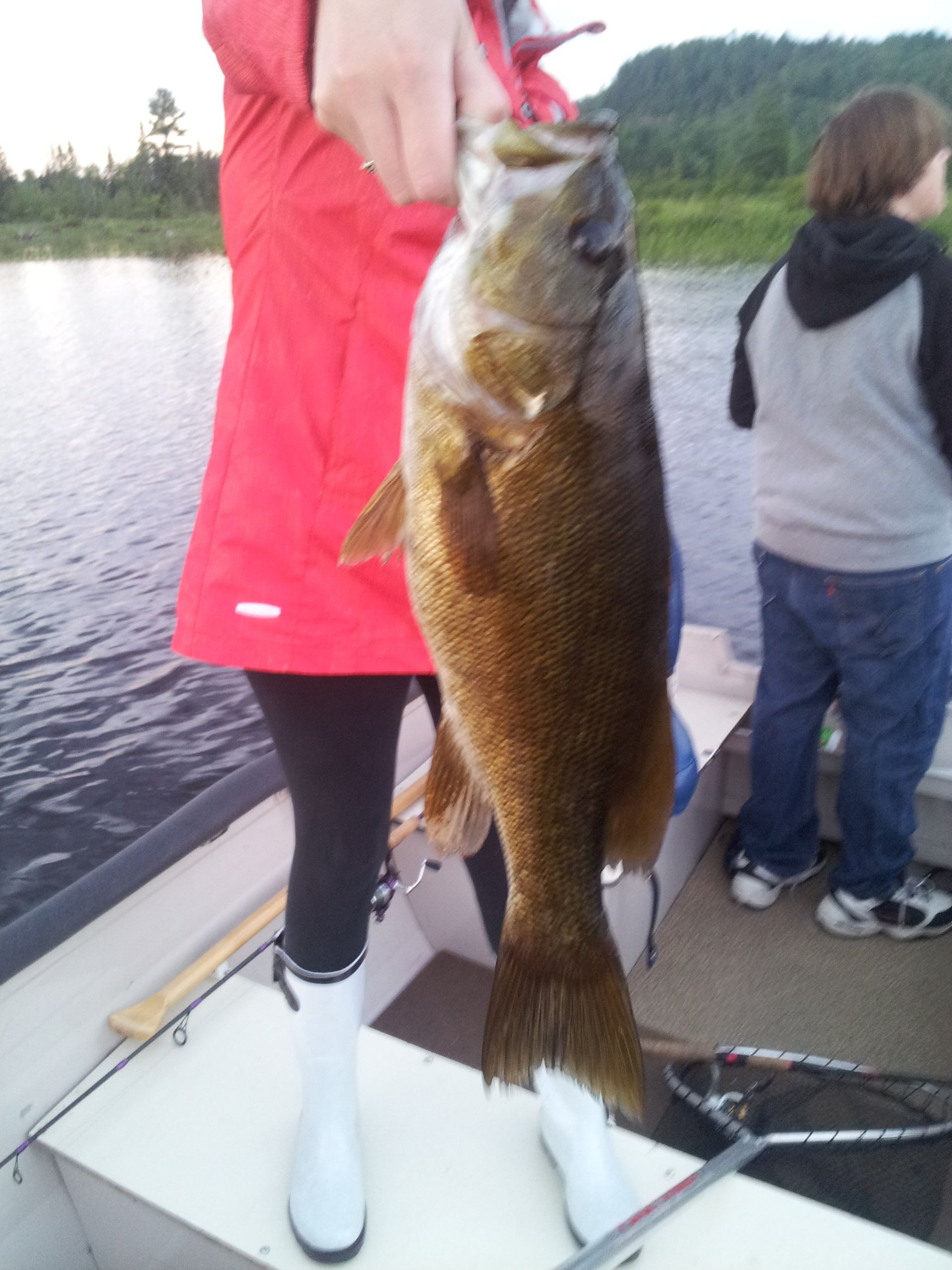A woman in a red jacket is holding a fish on a boat