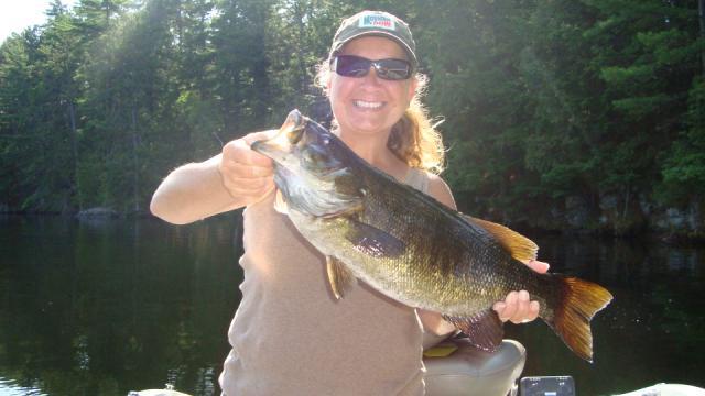 A woman is holding a large bass in her hands.