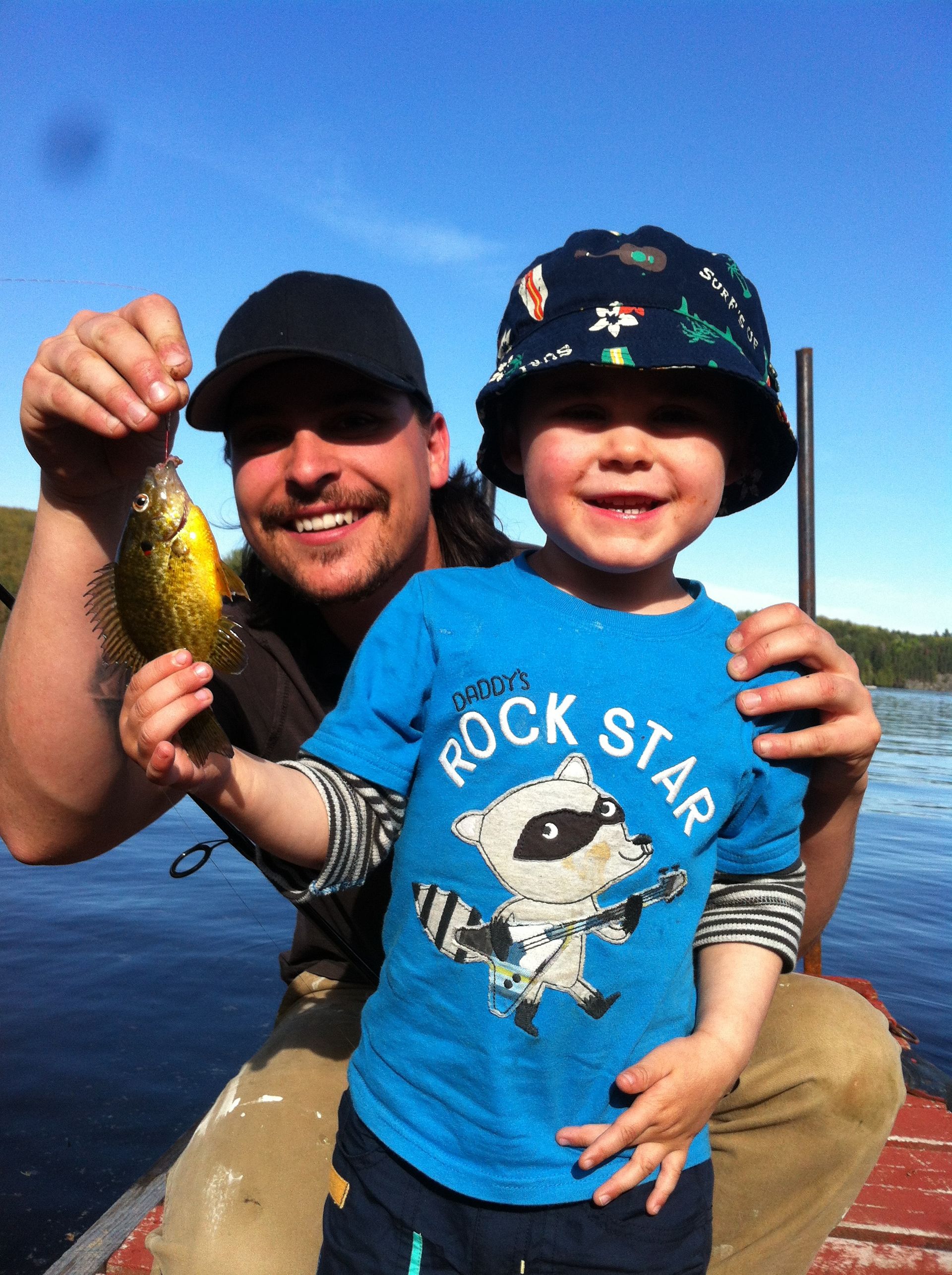 A little boy wearing a rock star shirt is holding a fish
