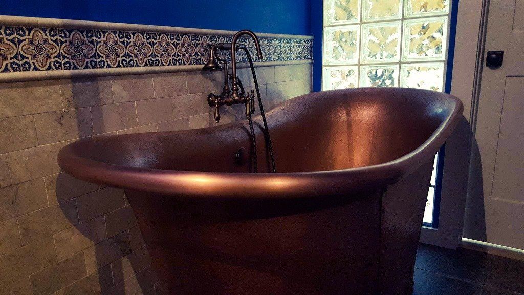 A copper bathtub in a bathroom with a blue wall