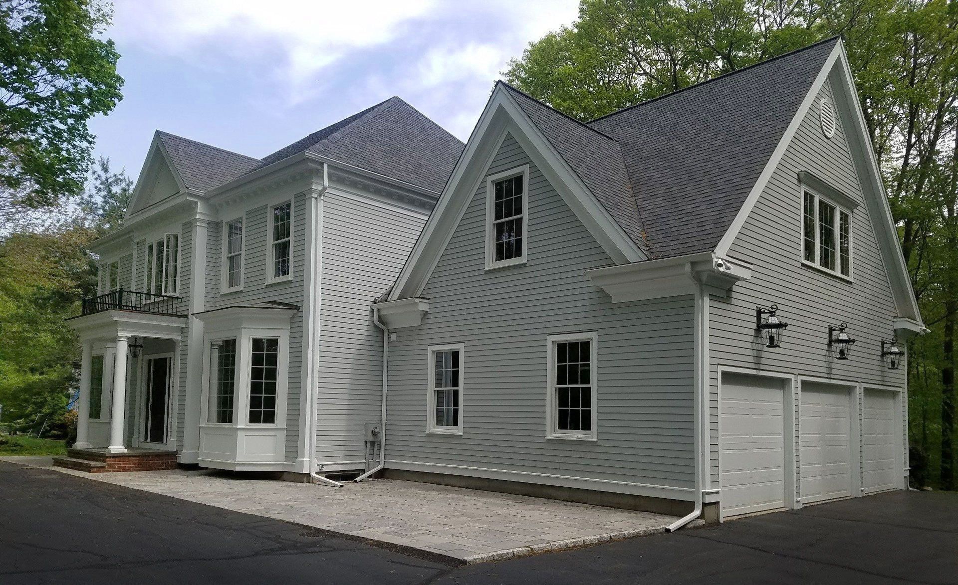 A large white house with a gray roof is surrounded by trees.