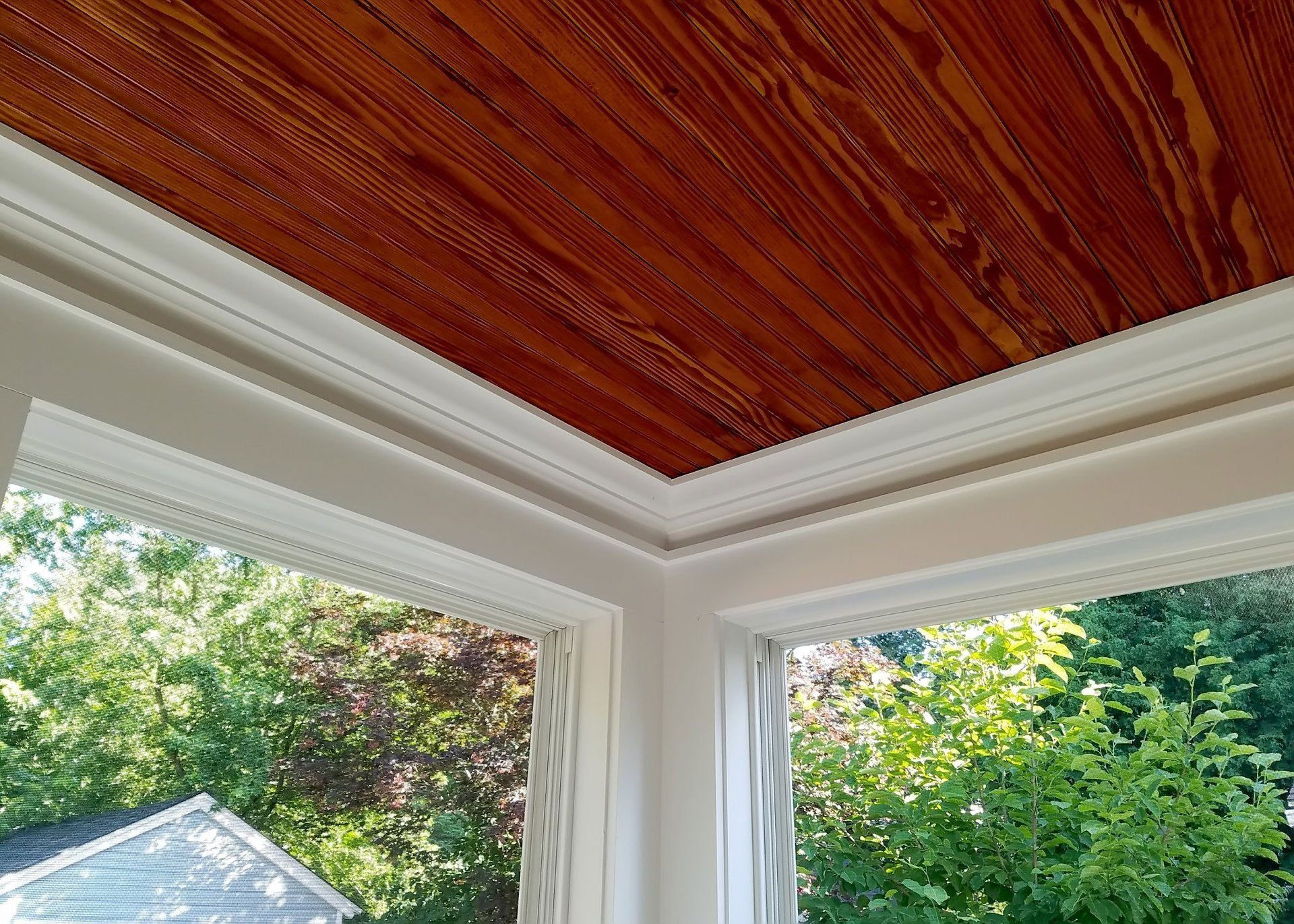 A room with a wooden ceiling and a window with trees in the background.
