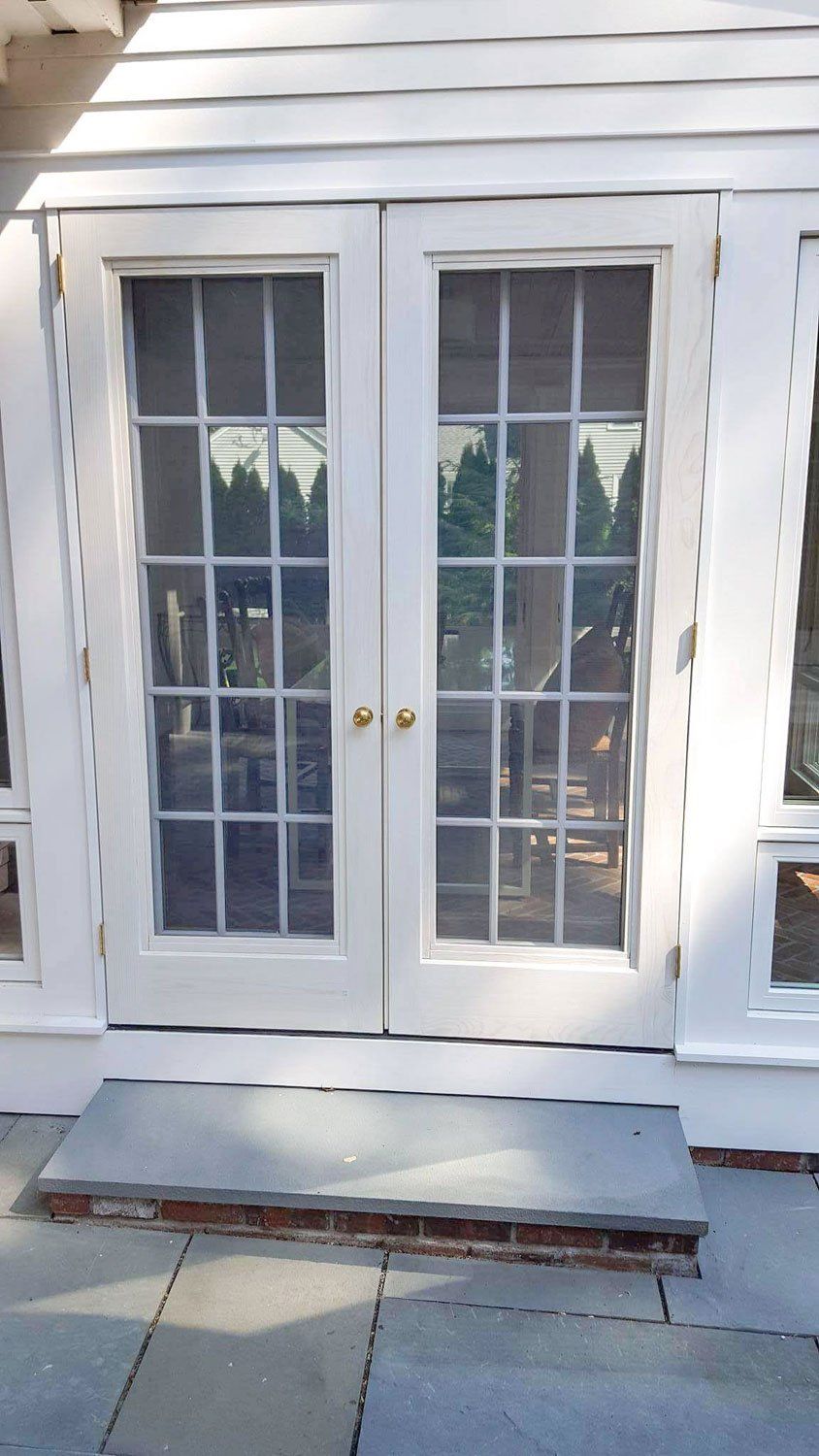 A white patio door with a reflection of trees in the glass.