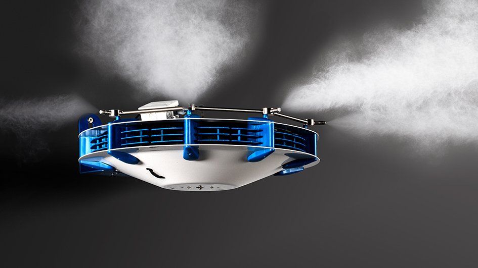 A suspended ceiling-mounted industrial misting system spraying a fine water fog in multiple directions.