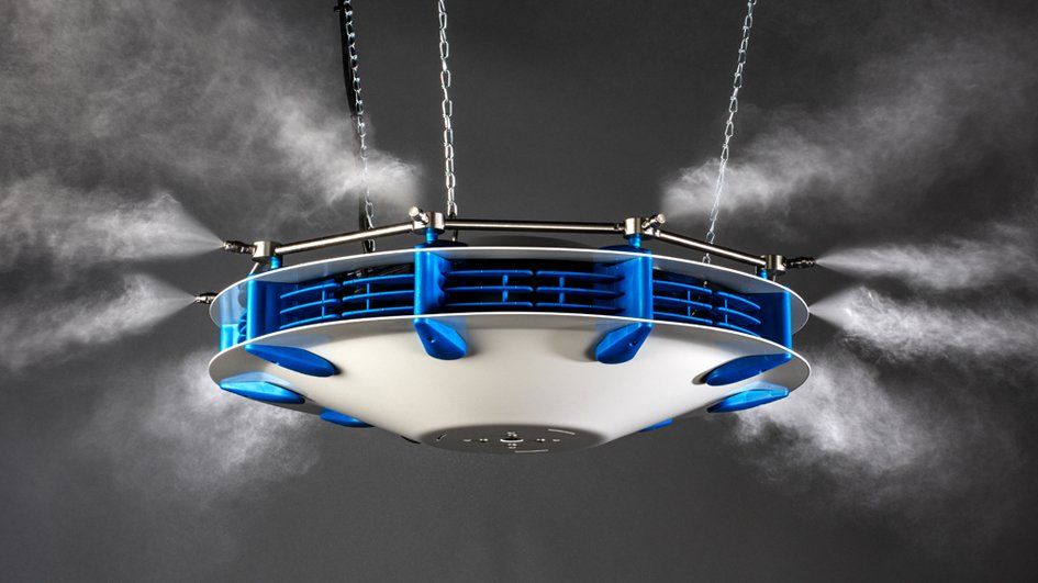 A suspended ceiling-mounted industrial misting system spraying a fine water fog in multiple directions.
