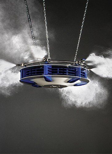 A suspended ceiling-mounted industrial misting system spraying a fine water fog in multiple directions.