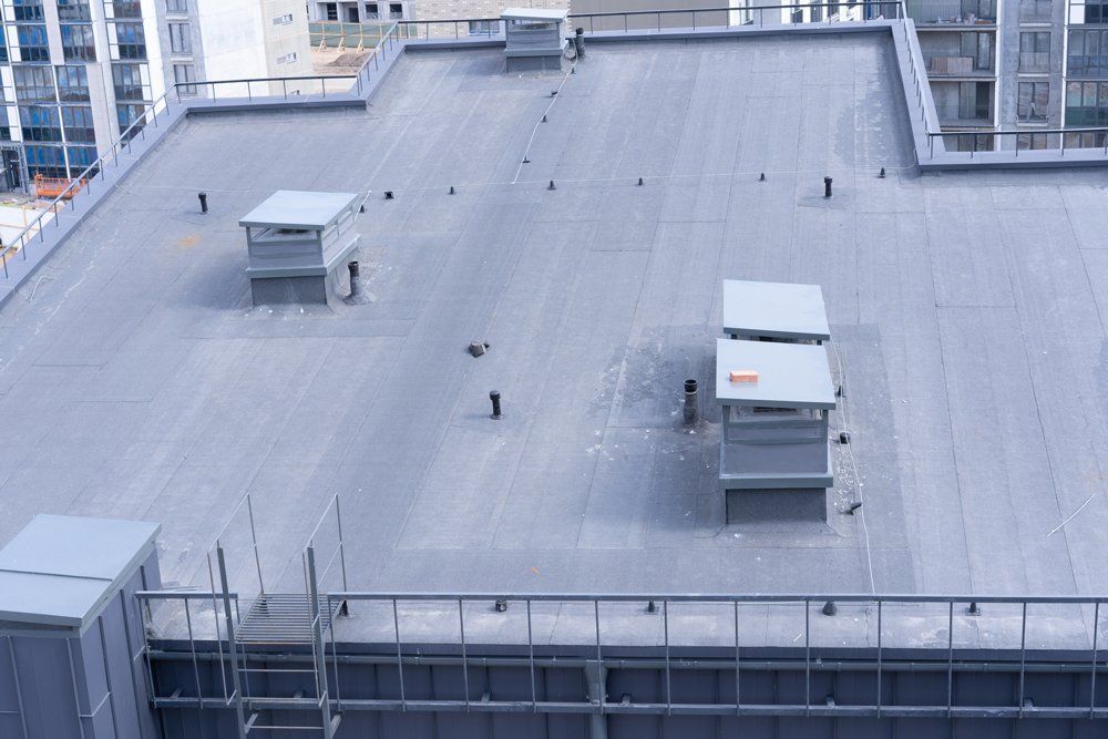 Flat, gray rooftop with several ventilation units and other structures. Buildings are in the background.