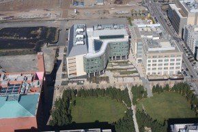 Aerial view of a modern building with a curved glass facade, surrounded by trees and a green lawn.